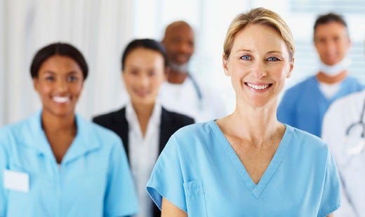 Mehrere Pflegefachkräfte stehen zusammen und lächeln in die Kamera.