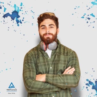 Junger Tischler steht nach seinem Berufsabschluss an der TÜV Rheinland Akademie stolz vor einer Wand