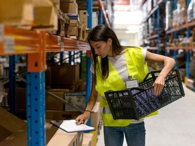 Mitarbeiter im Lager überprüft Bestände mit einem Klemmbrett vor einem Regal Eine Mitarbeiterin im Lager sortiert die Waren und überprüft die Notizen auf einem Klemmbrett