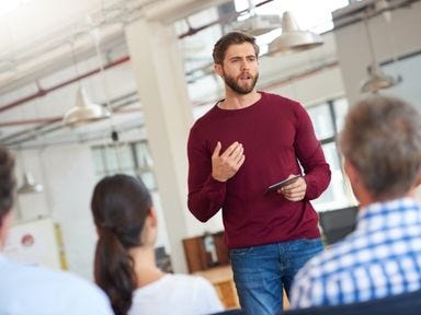 Hartz 4 und Bürgergeld: Wo sind die Unterschiede? Junger Mann mit weinrotem Pullover erklärt einer Gruppe den Unterschied zwischen Hartz 4 und Bürgergeld
