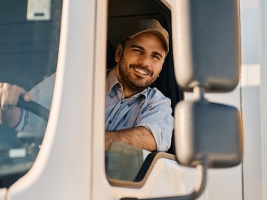 Ausländischer LKW Fahrer startet seine Tour  LKW Fahrer schaut aus dem Fenster seines LKWs und lächelt