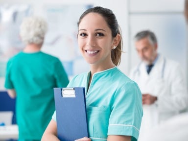 Pflegekraft steht in einer hellen Arztpraxis und lächelt in die Kamera