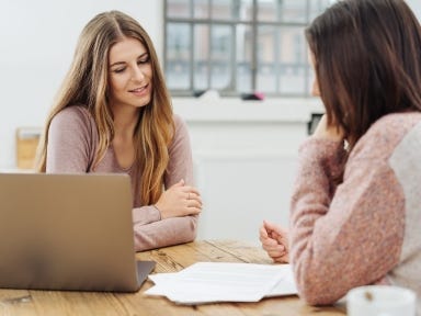 Zwei Frauen sitzen in einem hellen Raum an einem Holztisch
