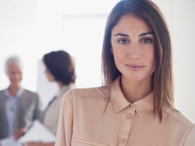 Frau mit steht in einem hellen Büro und schaut lächelnd in die Kamera.