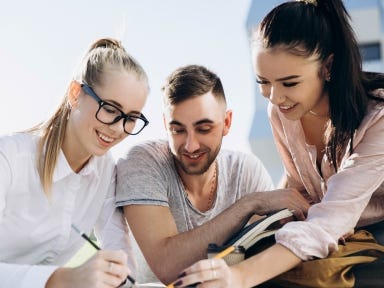 Eine Gruppe junger Menschen sitzen an einem Tisch und erledigen schriftliche Aufgaben zusammen