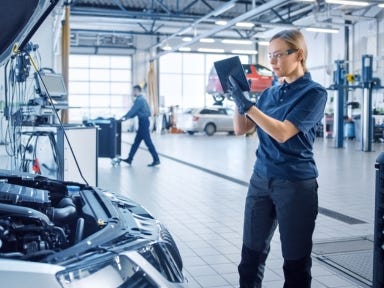 Ein Kfz-Mechanikerin arbeitet konzentriert in einer Autowerkstatt an einem Fahrzeugmotor.