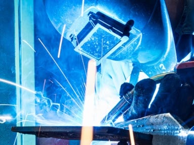 Ein Schweißer arbeitet mit Schutzhelm an einer Metallkonstruktion und erzeugt Funkenflug.