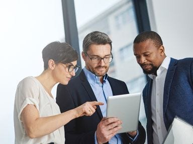 Ein internationales Team schaut gemeinsam auf ein Tablet und bespricht eine Lösung.