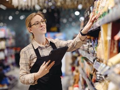 Eine Verkäuferin überprüft mit Hilfe eines Tablets die Waren im Regal eines Supermarktes