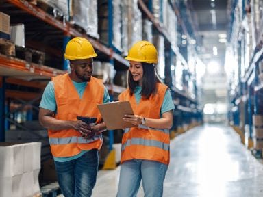 Ein Mann und eine Frau stehen in einem Hochregallager und besprechen den weiteren Arbeitsschritt