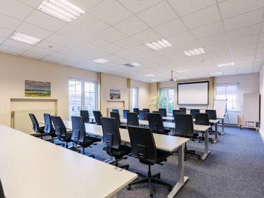 Ein Seminarraum mit vielen Stühlen und Tischen un einer Leinwand im Hintergrund