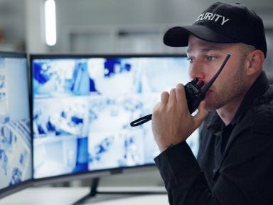 Ein Mann &uuml;berwacht in einer Sicherheitszentrale die Geb&auml;ude &uuml;ber den Monitoren