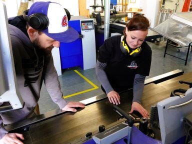 Eine Frau und ein Mann stehen vor einer Werkbank in einer Tischlerwerkstatt
