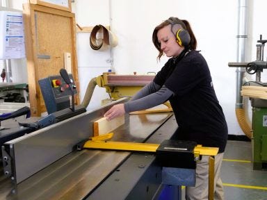 Eine Frau schneidet an einer Maschine ein Stück Holz durch