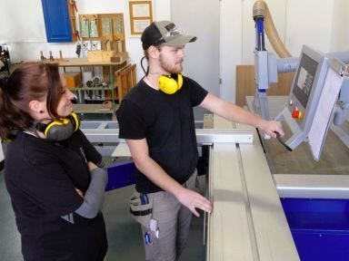 Eine Frau und ein Mann stehen in einer Holzwerkstatt an einer Maschine