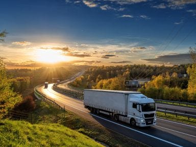 Auf einer Autobahn fährt ein LKW, während sich der Sonnenuntergang am Horizont zeigt.