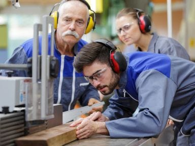 Ein Ausbilder zeigt zwei Azubis in einer Metallwerkstatt wi eman ein Werkst&uuml;ck bearbeitet