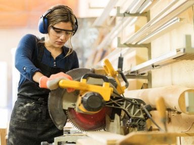 Eine Umschülerin steht an einer Werkbank mit einer Kreissäge in einer Holzwerkstatt