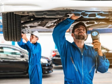 Kfz-Mechatroniker bei der Wartung eines Fahrzeugs in einer modernen Werkstatt