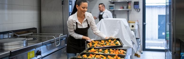 Koch wird von Küchenhelferin bei der Arbeiit unterstützt Koch wird von Küchenhelferin bei der Arbeiit unterstützt