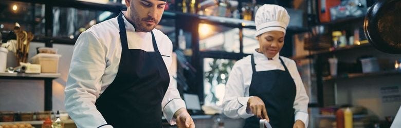 Ein Koch und eine Köchin bereiten Essen in einem Restaurant zu. Ein Koch und eine Köchin bereiten Essen in einem Restaurant zu.