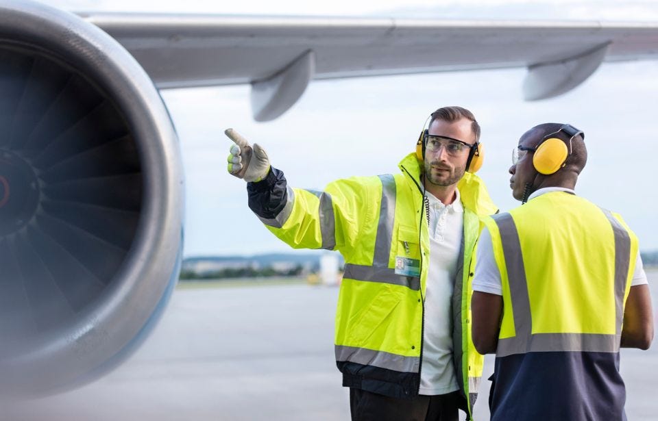 Zwei Mitarbeiter des Bodenpersonals befinden sich neben einem Flugzeug.