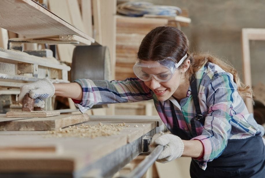Eine junge Frau mit Schutzbrille arbeitet an einer Werkbank.