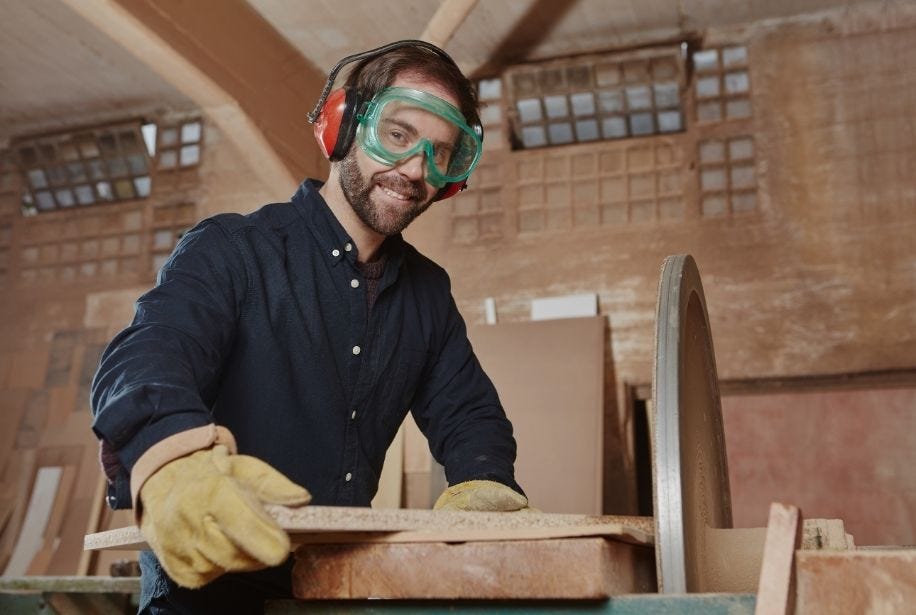 Ein Mann mit Schutzbrille und Geh&ouml;rschutz arbeitet an einem Holzprojekt.