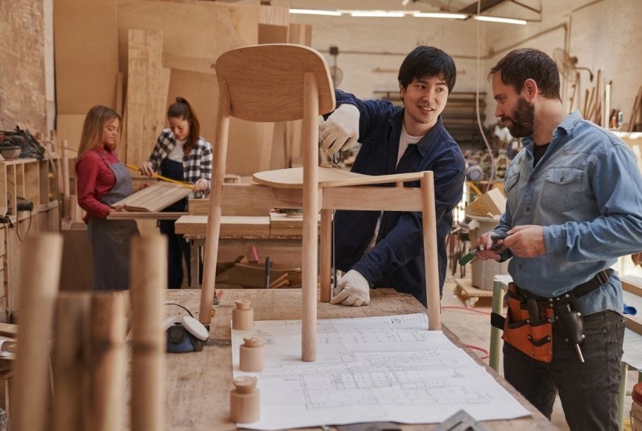 Zwei M&auml;nner bauen einen Stuhl aus Holz zusammen.