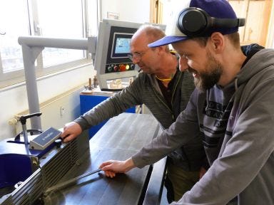 Ein Ausbilder erklärt einem Umschüler die Maschine in einer Holzwerkstatt