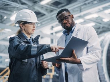 Facharbeiterin erklärt einem Kollegen in einer Fabrik einen Arbeitsschritt