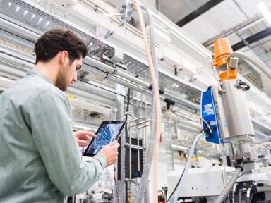 Industriearbeiter überprüft Produktionsdaten auf einem Tablet in einer Fabrikhalle