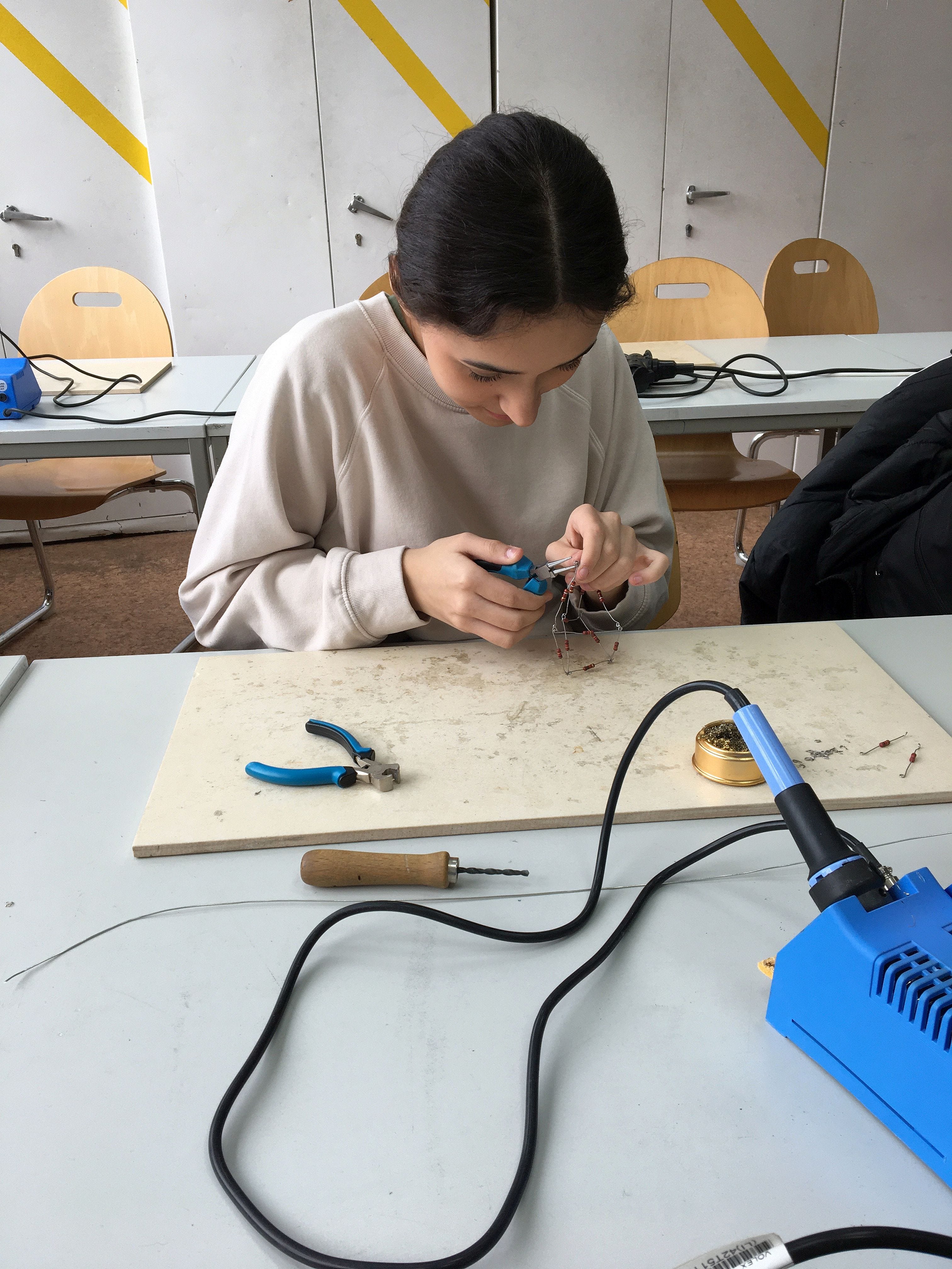 Eine Schülerin knipst mit einer Zange Metalldrahte zusammen