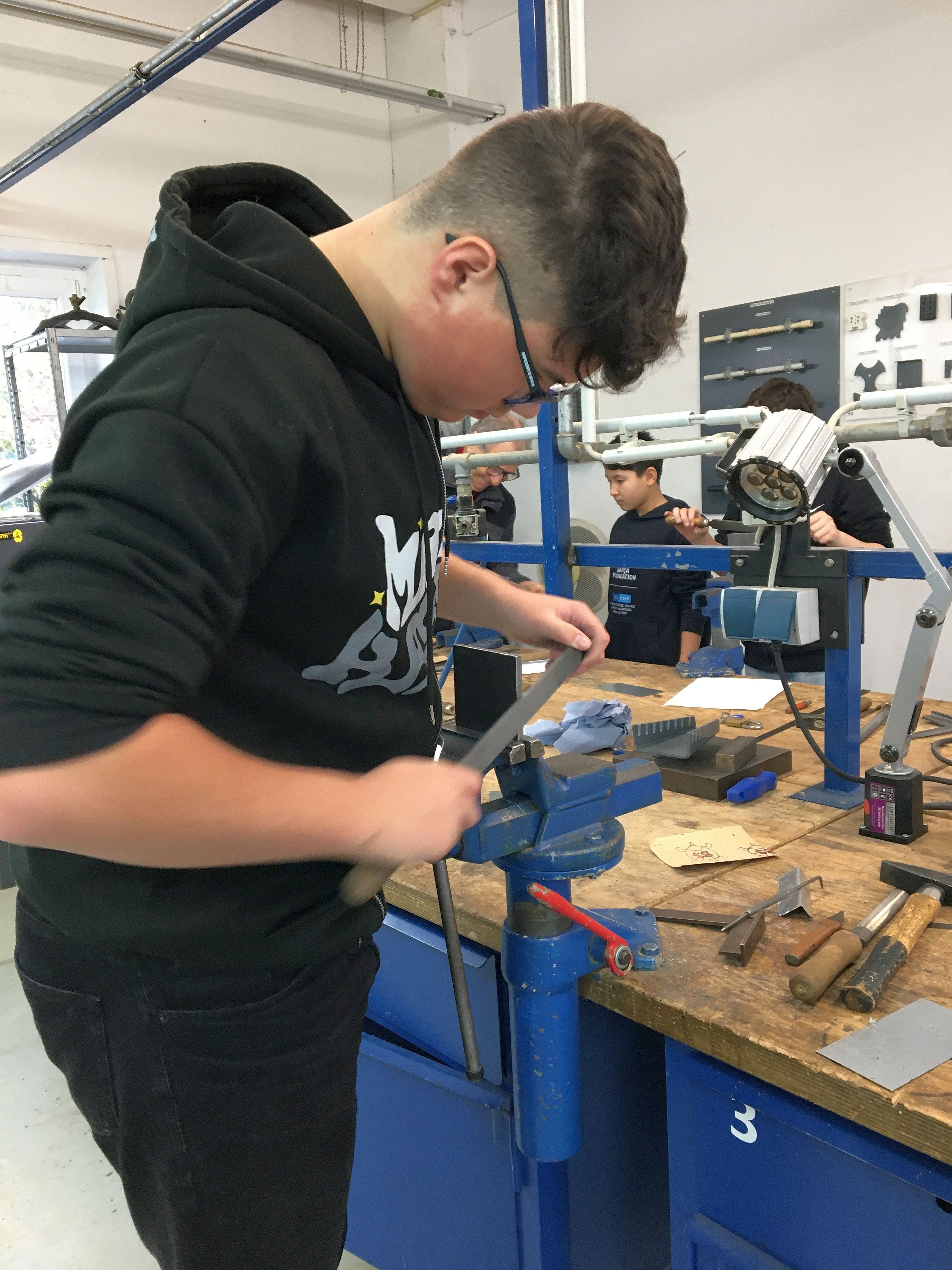 Ein Schüler schleift mit einer Pfeile an einem Metallstück 