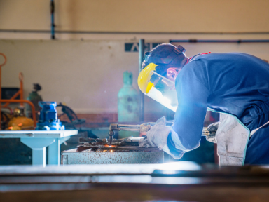 Junger Schwei&szlig;er bei der praktischen Qualifizierung in einer Werkstatt mit Schutzausr&uuml;stung