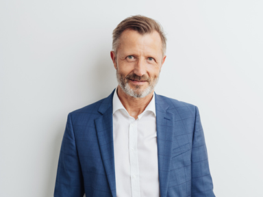 Matthias Werner, Geschäftsführer Autohaus Werner Geschäftsführer Matthias Werner steht lächelnd in einem blauen Anzug vor einer weißen Wand.