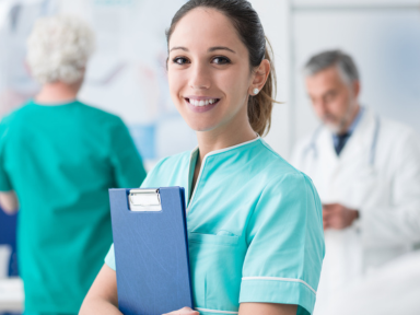 Pflegefachfrau in einem Klinikteam. Eine Pflegefachfrau steht in einem offen und hellen Raum und lächelt in die Kamera.