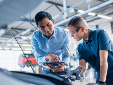Ausbilder zeigt einem Auszubildenden technische Details im Motorraum eines Autos &ndash; Ausbildung im Kfz-Bereich