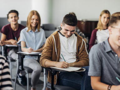 Prüfungsvorbereitung für Auszubildende Junge Auszubildende sitzen lachend in einem Klassenraum und schreiben – symbolisiert eine positive Prüfungsvorbereitung.