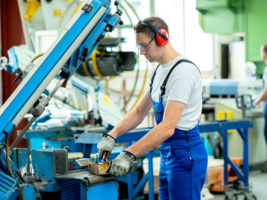 Ein Auszubildender bedient konzentriert eine Metallfräsmaschine in einer industriellen Fertigungshalle.